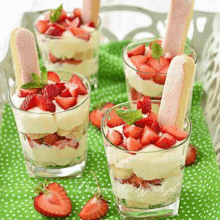 four glasses filled with strawberries and whipped cream on a green table cloth