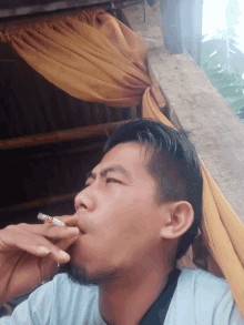 a man is smoking a cigarette with a yellow curtain behind him