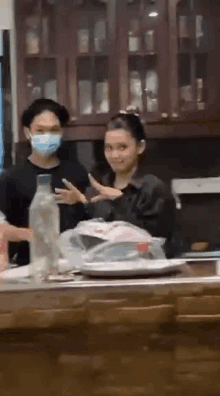 a woman wearing a mask is standing in a kitchen next to a man .