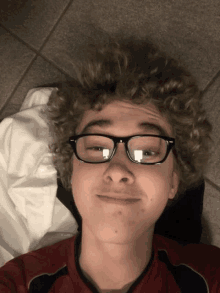 a young man with curly hair wearing glasses laying on the floor