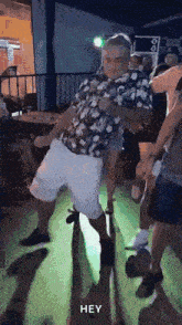 a man in a floral shirt and white shorts is dancing on a dance floor with other people .