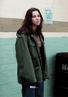 a woman in a green jacket is standing in front of a brick wall with a sign on it that says " support the peace club "