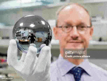 a man in a white glove is holding a glass ball with a reflection of himself in it .