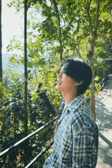 a man in a plaid shirt is standing in front of trees on a path