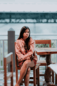 a girl wearing a pink hoodie with a mountain on it sits at a wooden table