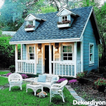 a small blue and white playhouse with a porch and a table and chairs