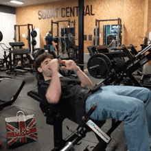 a man sits on a machine in a gym with the words squat central on the wall behind him