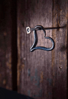 a wrought iron hook in the shape of a heart is hanging on a wooden wall .