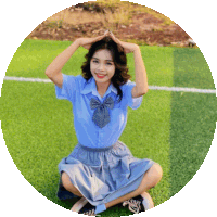 a girl in a blue shirt and skirt is kneeling on the grass