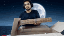 a man wearing headphones is holding a cardboard box in front of a full moon