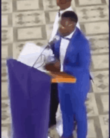 a man in a blue suit is standing at a podium holding a bible .