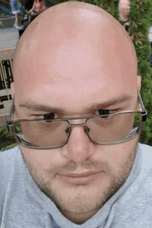 a bald man wearing glasses and a grey shirt