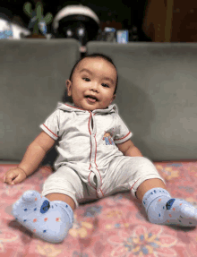 a baby is sitting on a pink blanket and wearing blue socks with the letter e on them