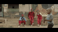 a group of men in red overalls are sitting on a brick wall while a boy stands in front of them