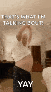 a man with a big belly is standing in a living room with his arms up .