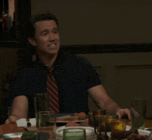 a man in a blue shirt and red tie sits at a table with plates of food