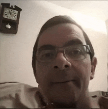 a man wearing glasses is smiling in front of a pendulum clock hanging on a wall .