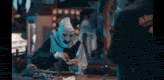 a man in a clown costume is sitting at a table with a bottle of alcohol