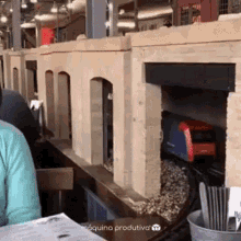 a woman sits at a table in front of a model train and a sign that says " maquina produtiva "