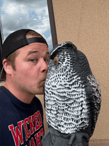 a man in a wicked shirt kisses an owl statue