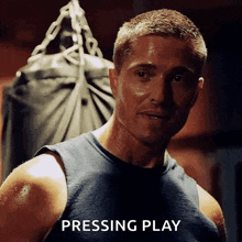 a man in a tank top is standing in front of a punching bag and the word pressing play is below him