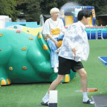 a couple of men are standing next to each other in a park . one of the men is sitting on a climbing wall .