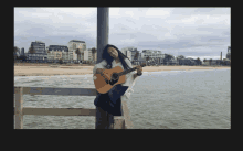 a woman leans against a pole holding a guitar