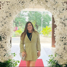 a woman in a green jacket is standing in front of a white flower arch