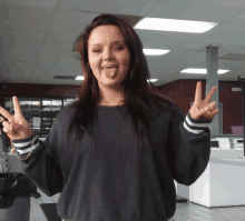 a woman in a grey sweater is giving a peace sign