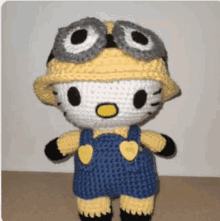 a crocheted hello kitty doll dressed as a minion wearing a hat and goggles .