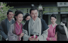 a group of people in traditional chinese clothing are standing in front of a building with chinese writing on it .