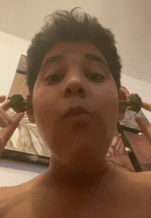 a shirtless boy is holding broccoli in front of his face