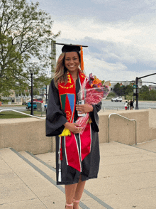 a woman in a graduation cap and gown is holding flowers