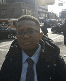 a young man wearing glasses and a jacket is standing on a street corner