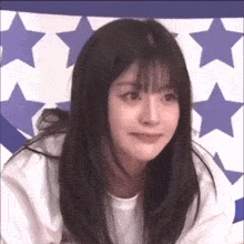 a girl with long hair and bangs is making a funny face in front of a blue and white star blanket .