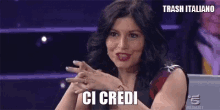 a woman is sitting in a chair with her hands folded and the words ci credi above her .