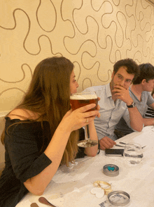 a woman drinking a glass of beer while sitting at a table with other people