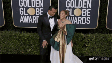 a man in a tuxedo and a woman in a dress pose on a red carpet in front of a golden globe award sign