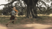 a man is running in a park with a frisbee in his hand and a tree in the background .