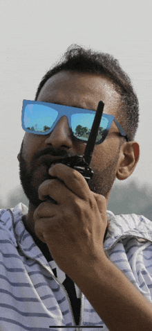 a man wearing sunglasses holds a walkie talkie in his hand