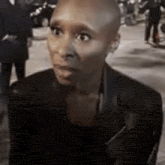 a bald woman wearing a black jacket is standing in a crowd of people .