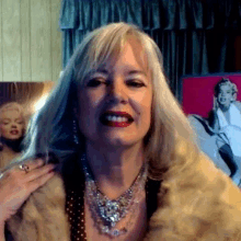 a woman wearing a fur coat and a necklace is smiling in front of a marilyn monroe painting .