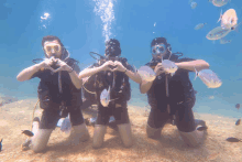 three scuba divers make a heart with their hands