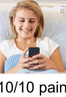 a young woman is laying in a hospital bed looking at her cell phone .