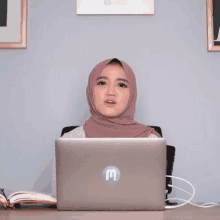 a woman in a hijab sits in front of a laptop with the words " gak enak " above her head