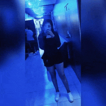 a woman taking a picture of herself in a hallway with blue lights behind her