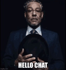 a man in a suit and tie is holding a hat in his hands and says `` hello chat '' .