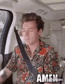 harry styles is sitting in the back seat of a car with his eyes closed and a seat belt .