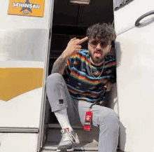 a man is sitting on the steps of a bus and making a funny face .