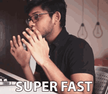 a man wearing glasses and a black shirt is sitting at a desk with the words super fast written on it